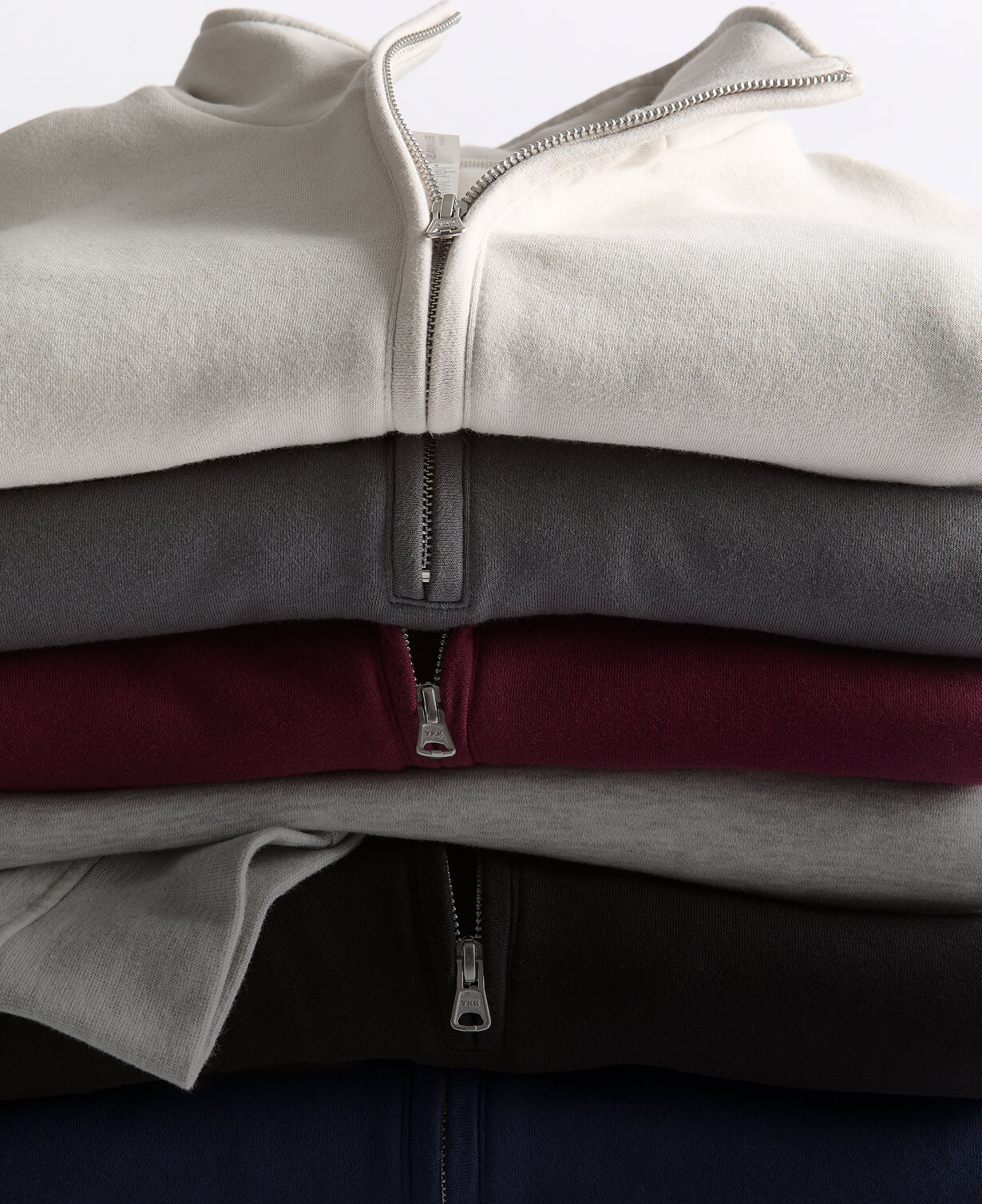 Stack of folded Women's Half-Zip Pullovers in cream, gray, burgundy, black, and navy.