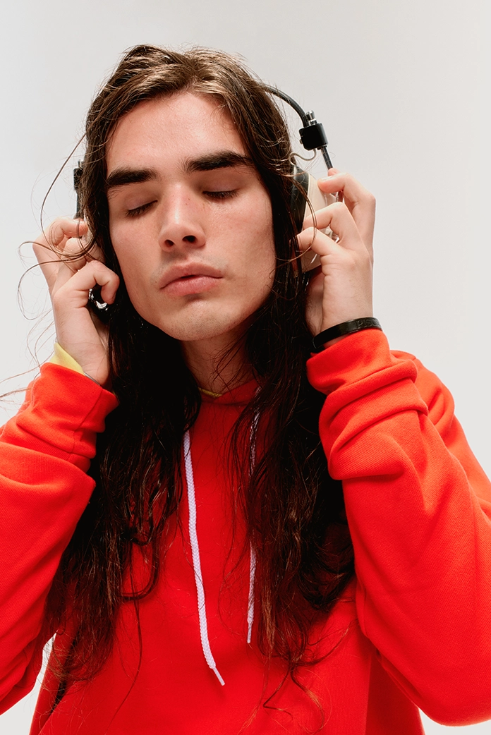 musician listens to music through headphones with eyes closed, wearing a poppy red hoodie with white drawstrings