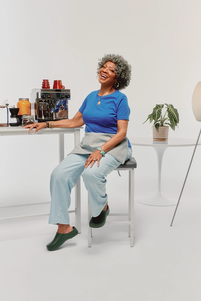 A barista wearing a true royal blue t-shirt sits on a stool in front of the espresso machine