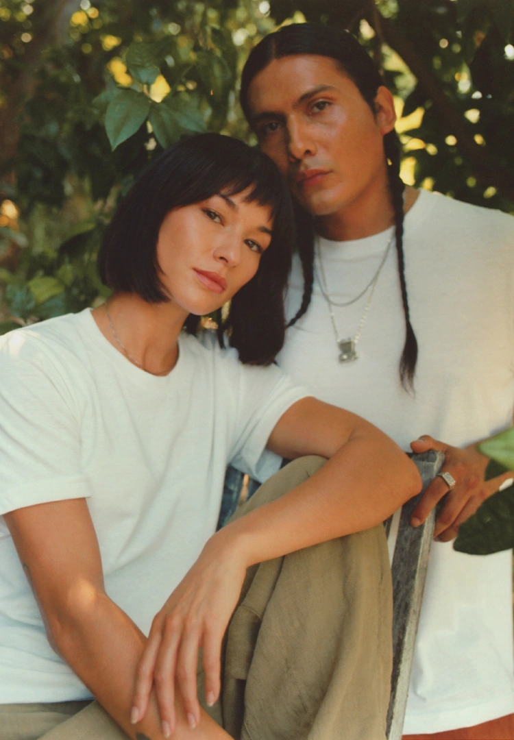 People are facing the camera wearing a crisp white t-shirt with greenery surrounding them
